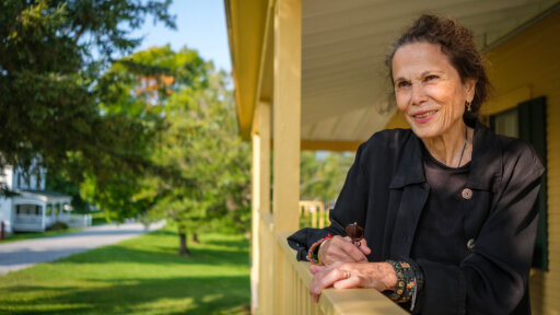 Writer Julia Alvarez standing on a porch smiling.